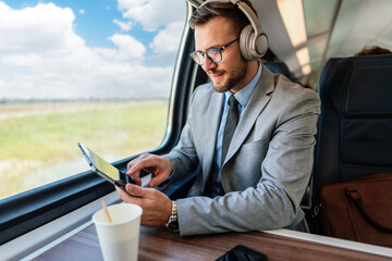 Young businessman wearing headphones and using digital tablet while traveling by train, enjoying music and staying productive during his commute