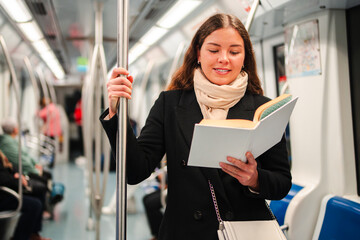 An enthusiastic woman engrossed in an intriguing book while standing on a subway train, fully absorbed in her reading experience and passing the time delightfully during her commute to work or school