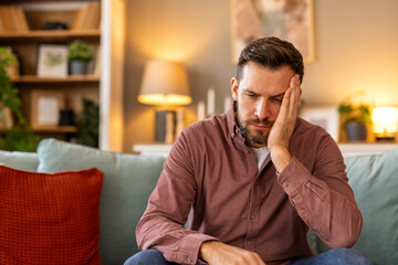 Obraz premium Closeup of man suffering from headache at home, touching his temples, copy space, blurred background. Migraine, headache, stress, tension problem, hangover concept