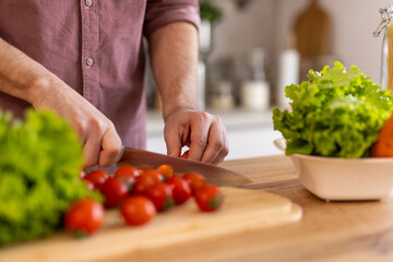 Man chopping vegetables in a kitchen, preparing ingredients for a meal. He is focused on the task, enjoying the process of cooking, with a relaxed and organized kitchen environment.
