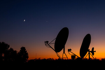 Satellite dishes silhouetted against vibrant sunset sky with crescent moon and Venus visible. Mediterranean region, Turkey