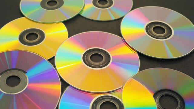 A row of CDs with different colors. The CDs are stacked on top of each other. The CDs are yellow, orange, and blue