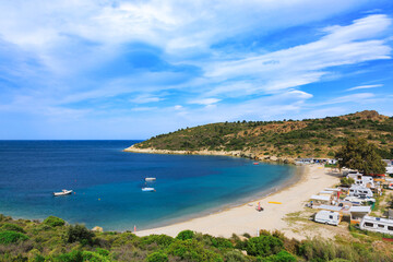 Coastal campground with caravans and boats on sandy beach along turquoise sea on summer day