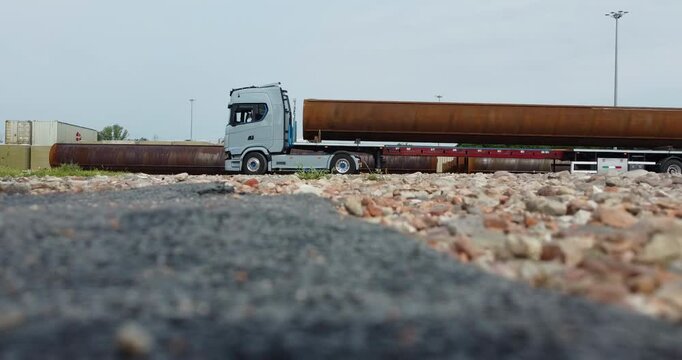 a truck makes a maneuver with a long trailer with a large steel pipe on top
