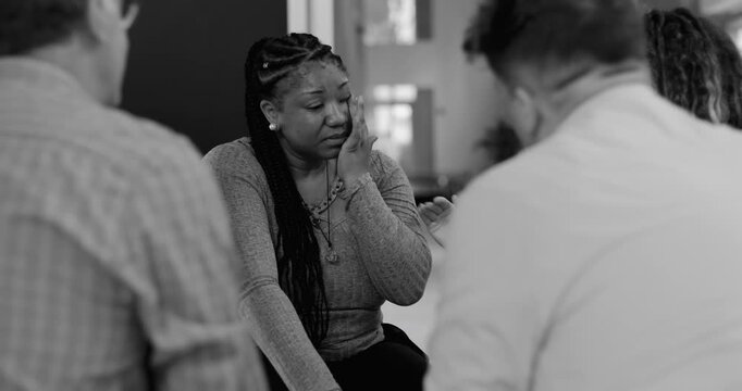 Woman crying during therapy session, receiving gentle touch from supportive group members in moment of deep vulnerability and shared empathy, black and white