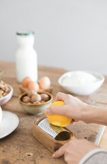 In a cozy kitchen, a hand grates fresh lemon zest over a wooden surface adorned with eggs, spices, and bowls of ingredients, creating a burst of flavor and creativity