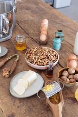 Bright lemon zest is being grated, surrounded by bowls of nuts, eggs, butter, and honey on a rustic wooden table, showcasing the art of baking and the joy of fresh ingredients
