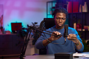 Young man seated in front of a professional microphone setup while recording podcast in a modern,...