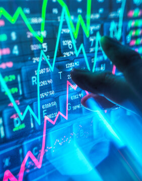 Hand touching a digital screen displaying stock market graphs and data