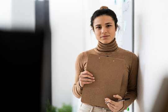 Female student with clipboard and pen leaning against wall