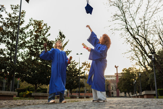 Two people celebrating graduation by tossing a cap on a university campus