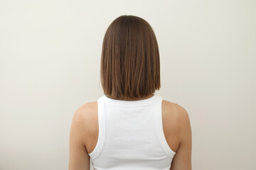 Rear view of young woman with straight shoulder length brown hair in white top on light background, emphasizing the hair texture and clean. Haircare, fashion, wellness, beauty, and lifestyle-related