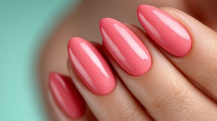 Close-up of a woman’s manicured hand with glossy coral pink nail polish on almond-shaped nails, set against a soft turquoise background