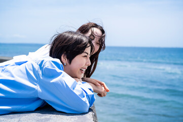 LGBTQ Couple or Close Female Friends Smiling Together While Leaning on a Seaside Wall Under Blue...
