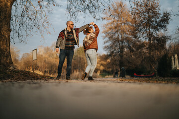 A joyful couple shares a dance in a serene autumn park, expressing romance and happiness. The surrounding fall foliage creates a warm, natural backdrop, complementing their connection and love.