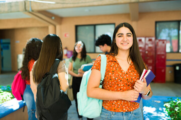 Smiling high school student carrying backpack and books on campus