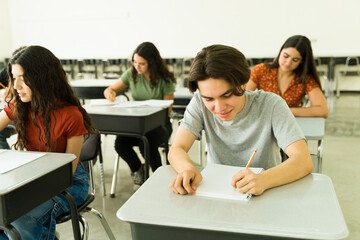 High school students taking exam in classroom: concentrated teenagers writing test