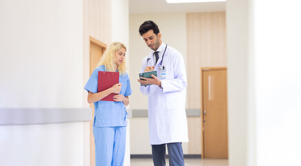Fototapeta premium Multi-ethnic healthcare workers in hospital. nurse and doctor walking in corridor and talking and in discussion for advice, medical service, diagnosis and consulting