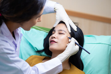 Fototapeta premium Facial aesthetics surgery treatment : Plastic (Cosmetic) Surgery Center : Brazilian hispanic female Doctor preparing Asian female patient for cosmetic surgery in clinic