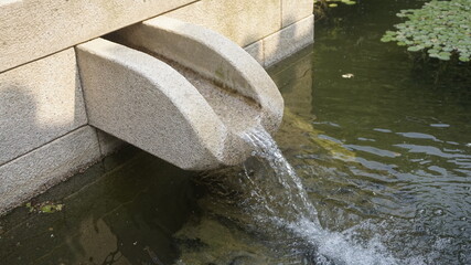 Close-up of crystal clear water cascading gently from a stone fountain into a calm pond.
