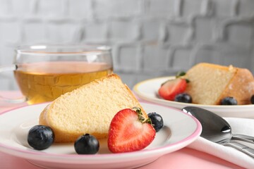 Pieces of tasty bundt cake with berries and tea on pink table, closeup