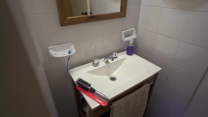Slow right motion camera clip inside white tiled restroom in cozy house, with large sink, mirror and some hair combs on top. Shot on 4K.