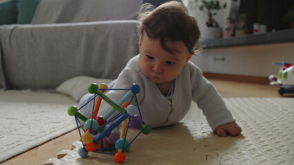 Baby playing with colorful toy on mat, developing motor skills through tactile exploration and...