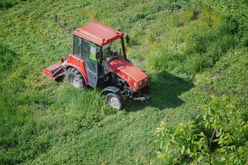 A red tractor with a mower in action among bright greenery — a symbol of summer activity and fruitful work in the fields. Ideal for seasonal publications.