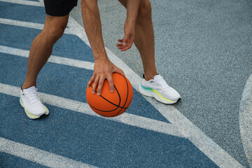 Naklejka premium Basketball player dribbling ball, capturing motion and shadow on blue outdoor court.