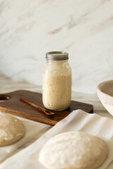 Freshly prepared sourdough bread dough rests on parchment near a container of active starter and a mixing bowl, showcasing the art of home baking.