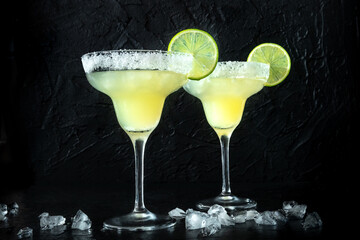 Margarita cocktail in classic glasses, side view on a black background, with lime and a salt rim, on ice
