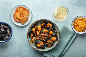Mussels with French fries, toast, lemon, and white wine, overhead flat lay shot on a blue stone background. Moules frites