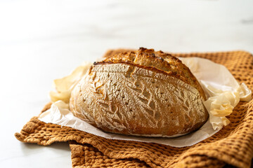 Crispy sourdough bread sits beside a glass jar filled with active starter, accompanied by a rustic cloth and a wooden board in a warm kitchen atmosphere.