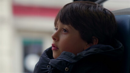 Young boy sitting by the window in a moving bus, lost in contemplation, deep in thought as he...