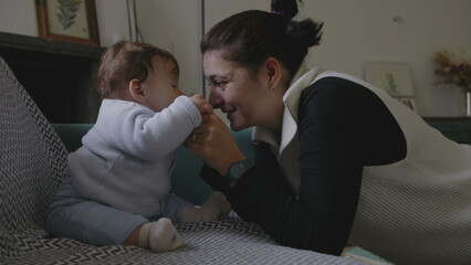 Mother interacting with baby on couch, engaging in playful face-to-face communication, showing joy...