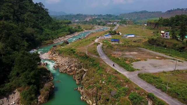 Aerial view of a turquoise river winding through a lush valley with dirt paths, small houses, and people. 