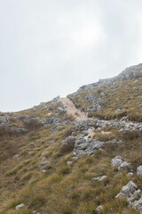 Rugged footpath climbs through uneven alpine terrain. Sharp stones and yellowing grass mark the remote wilderness route.