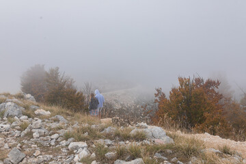 Misty mountain scene shows couple in hoodies walking downhill, surrounded by thick fog and sparse...