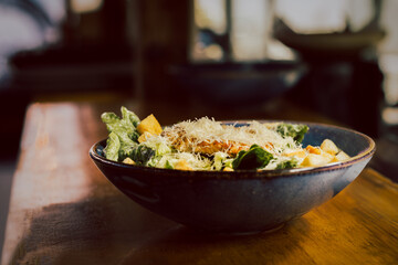Caesar salad with chicken and greens on wooden top in restaurant.