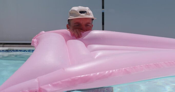 Man inflating air pink mattress in pool. 