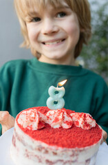 Cute blond happy boy holds a cake with a burning candle in the shape of number 8 and makes a wish....
