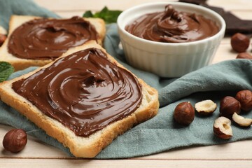 Toasts with chocolate hazelnut spread and nuts on wooden table, closeup