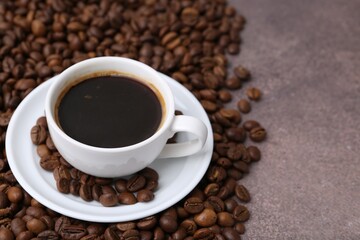 Aromatic coffee in cup, saucer and beans on brown textured table, closeup. Space for text