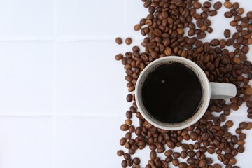 Aromatic coffee in cup and beans on white tiled table, flat lay. Space for text