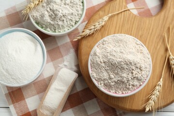 Different types of flour in bowls, scoop and spikes on table, flat lay