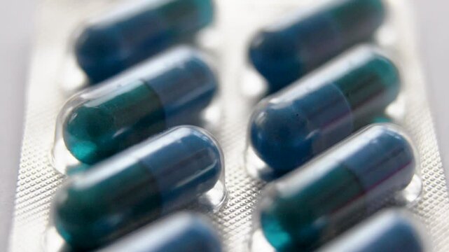 a very close-up vertical shot from top to bottom of an aluminium and plastic plate filled with hermetically sealed blue and dark green capsules
