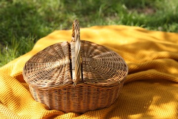 Wicker basket and blanket on green grass outdoors, closeup