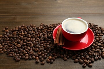 Aromatic coffee in cup, beans and cinnamon on wooden table, closeup