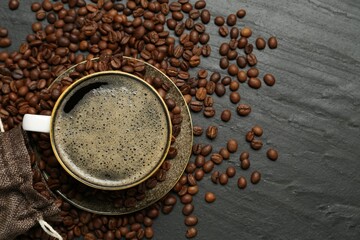 Aromatic coffee in cup and beans on black table, flat lay. Space for text