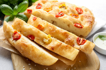 Cut delicious focaccia with tomatoes and basil on table, closeup
